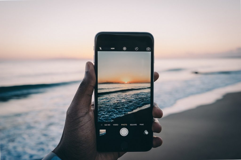 Una persona sosteniendo un teléfono para tomar una foto de la playa al atardecer.